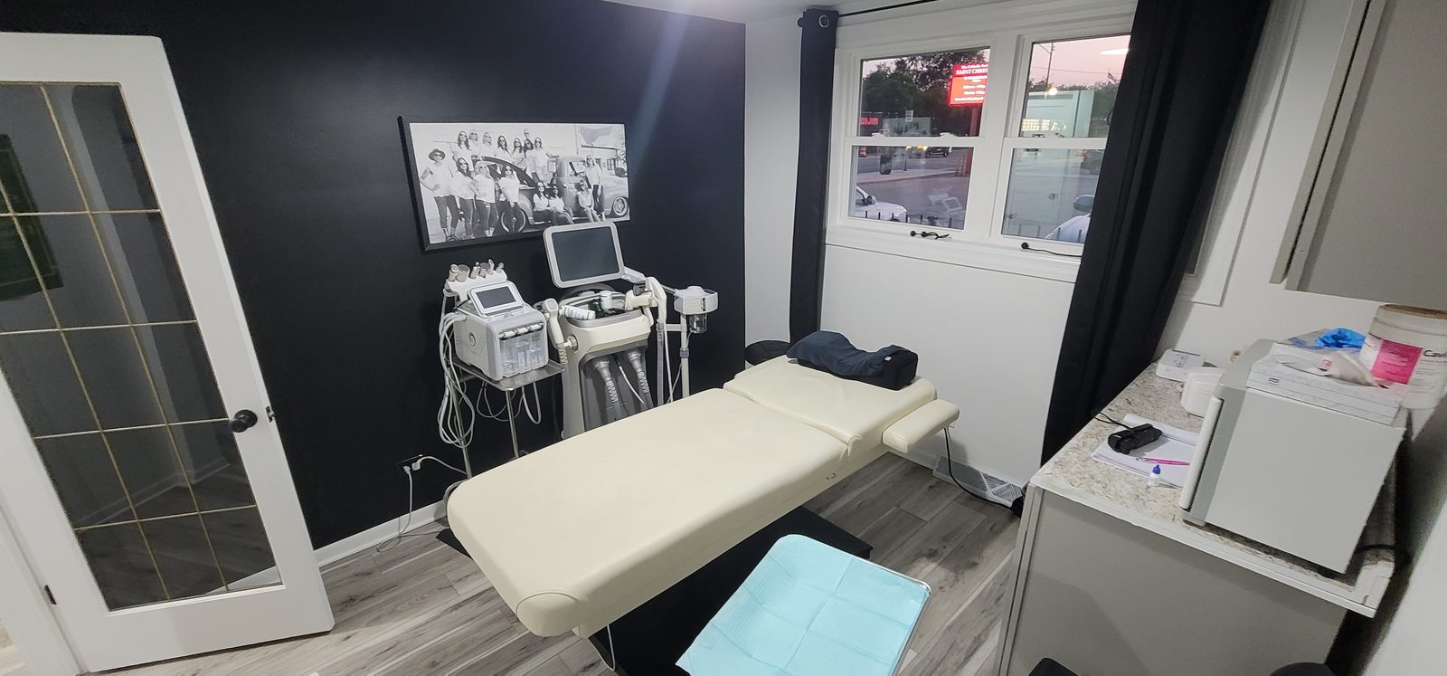 Treatment room with a white treatment table, device carts, a window and a black accent wall