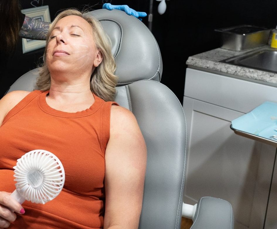 Relaxed patient in an orange top holding a small fan while reclining in a med spa treatment chair